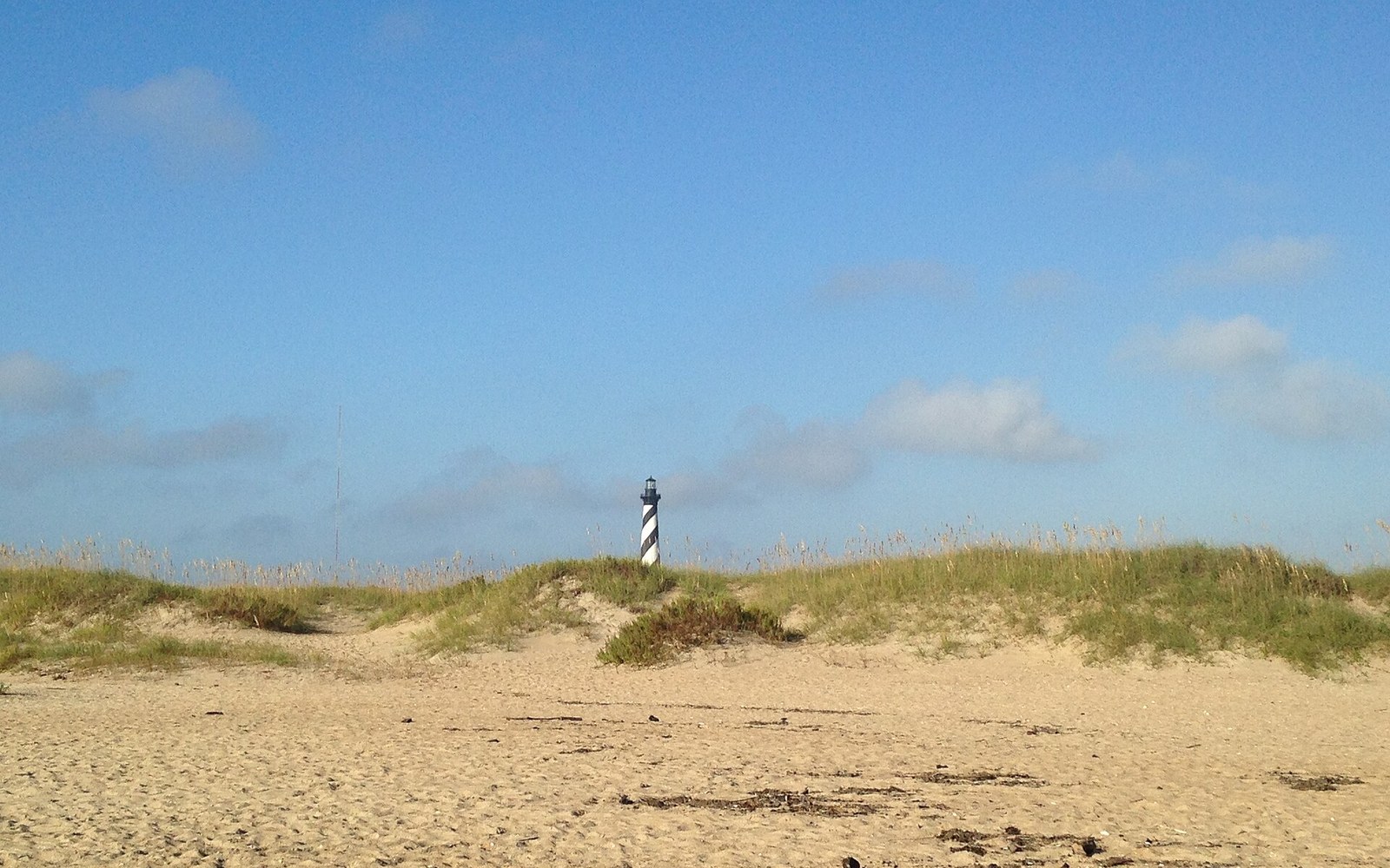 A striped lighthouse rising behind dune grass under flat coastal light