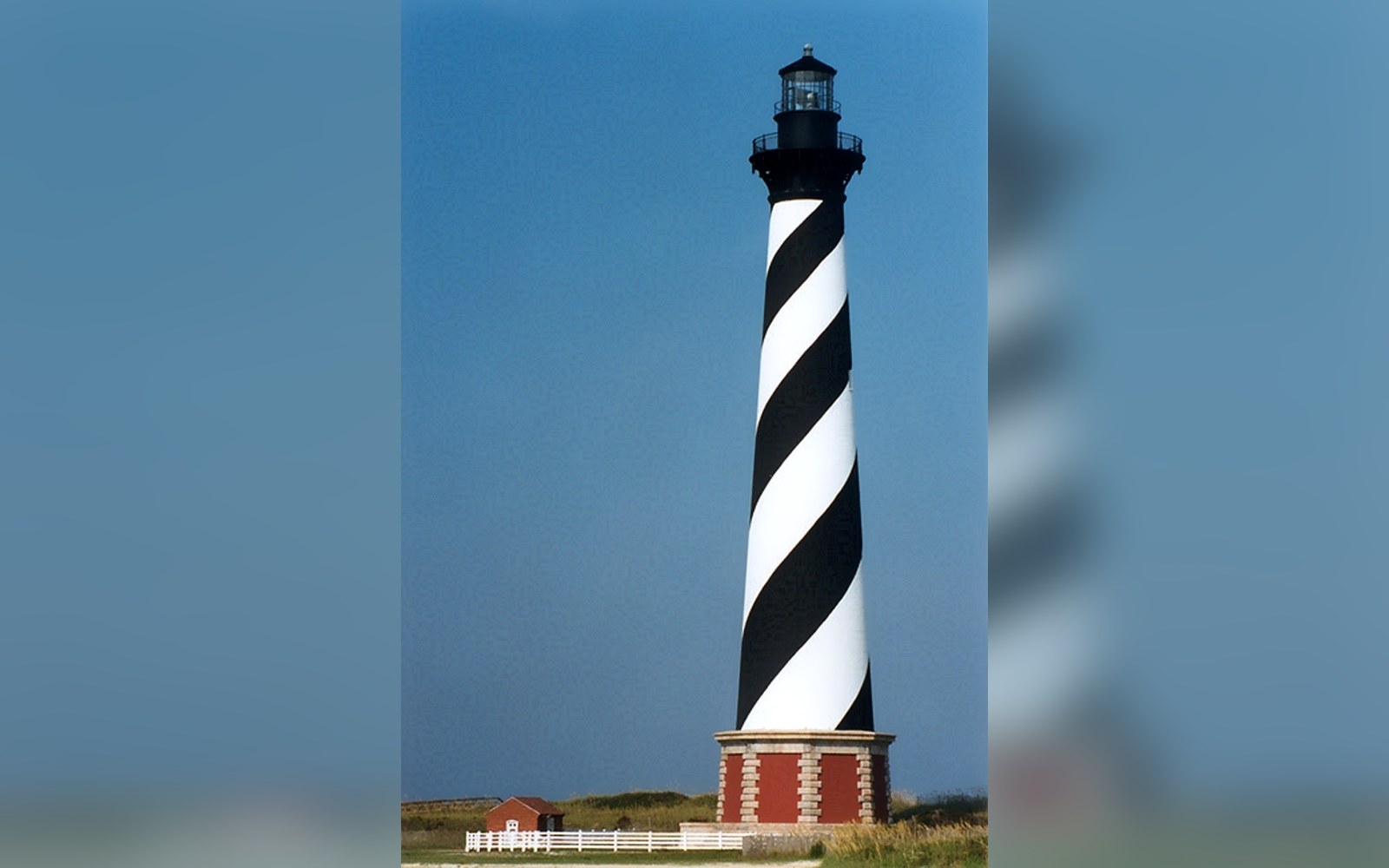 Black-and-white spiral striped lighthouse tower stands on a brick base under clear sky